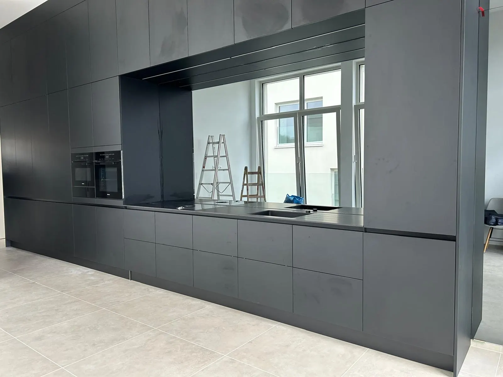 Grand miroir mural sur mesure en crédence dans une cuisine noire mate — Vitralux Bradtke Luxembourg