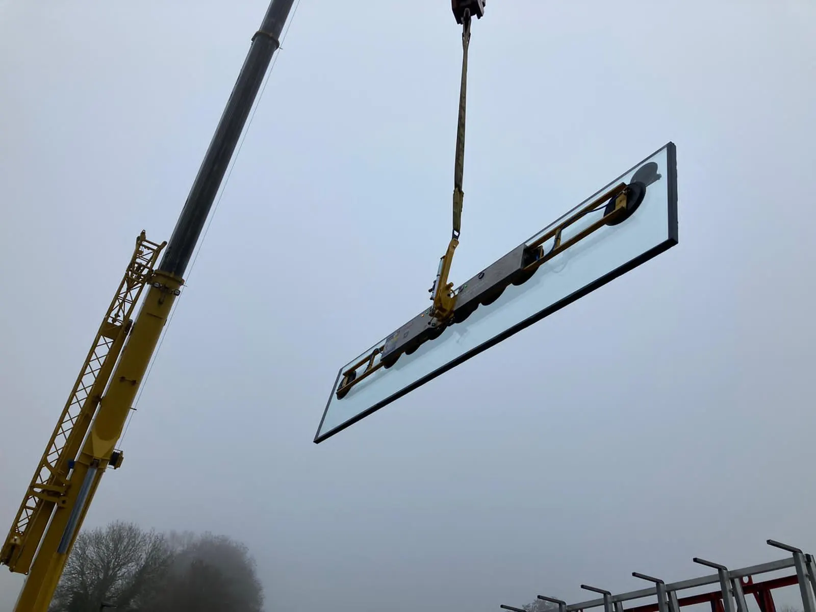 Paroi de verre grand format suspendue à la grue avant sa mise en place — vitrage de bassin sur mesure